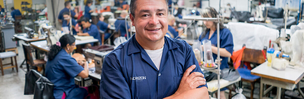 Happy adult Latin American man working at a shoe-making factory and looking at the camera smiling